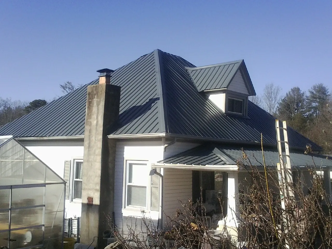 Dark blue standing seam metal roof on a white farmhouse with dormer — Slate & Tile Roof Repair by Roofing Brothers in Caney