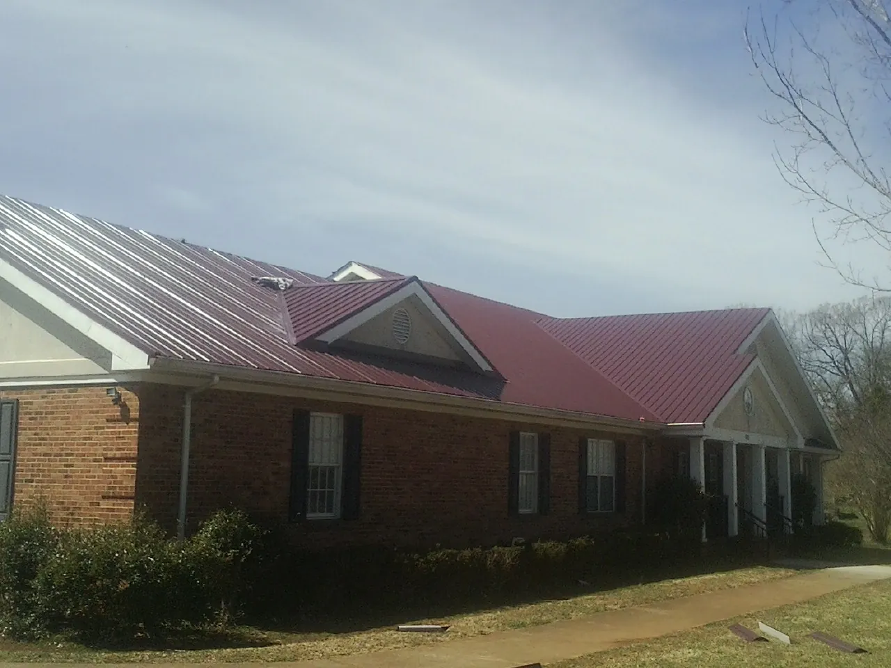 Red metal roof with gabled entries on a long brick building, from a Hail Damage Roof Repair job in Caney