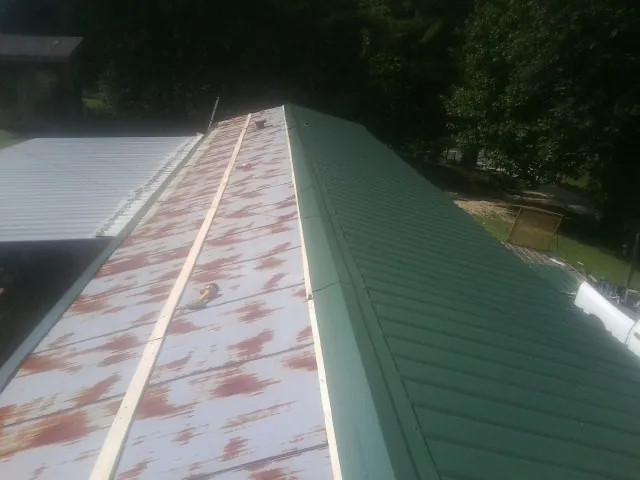 Old rusted panels beside newly installed green metal roofing — Wind Damage Roof Repair by Roofing Brothers in Caney