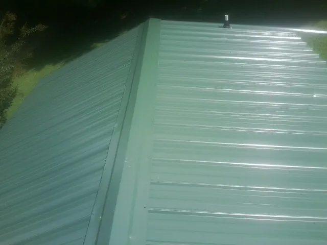 New green metal panels meeting at the ridge of a roof — Flat Roof Repair work by our crew in Caney