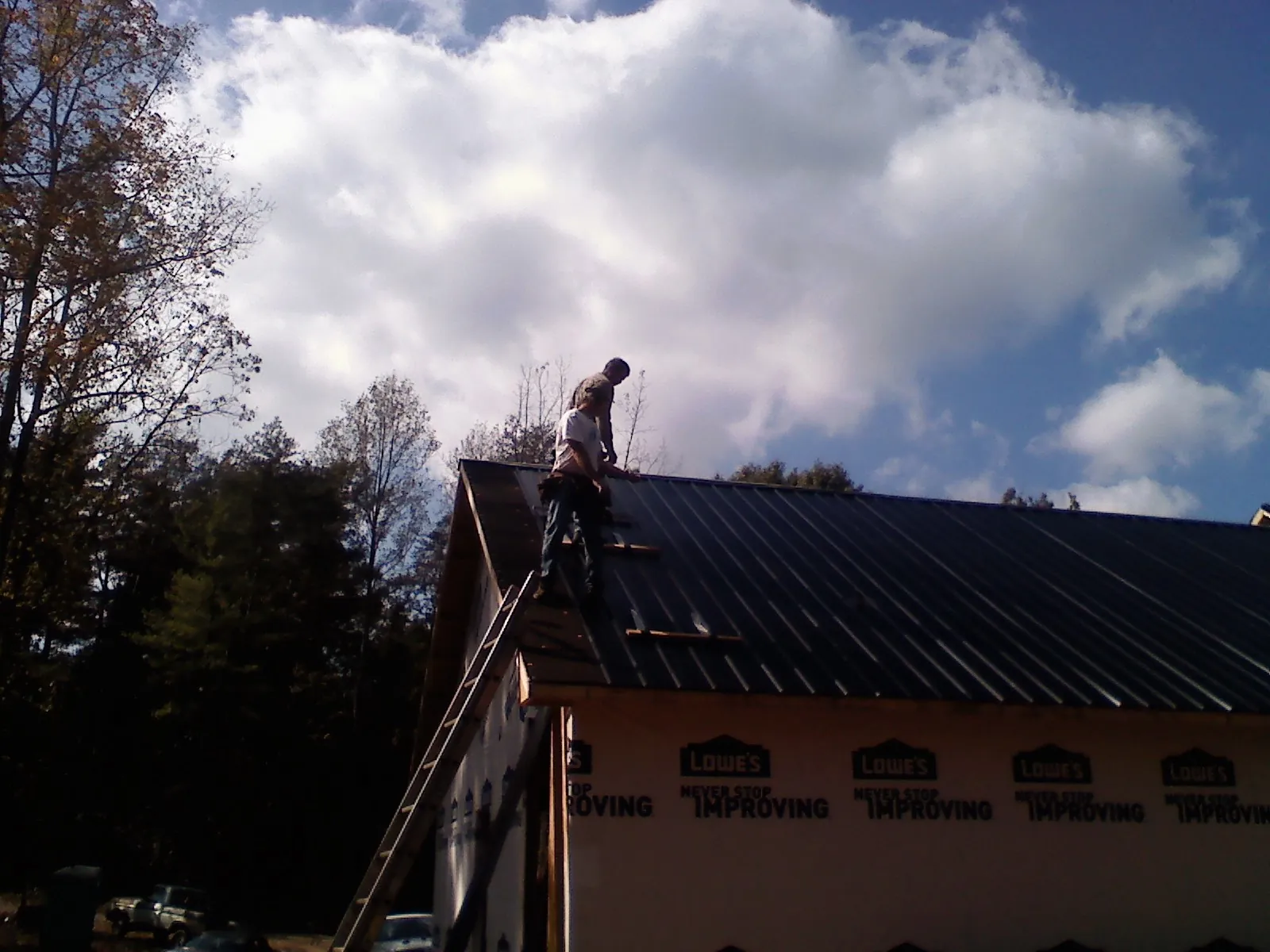 Roofer fastening dark metal panels high against a cloudy sky, from a Roof Inspection job in Caney