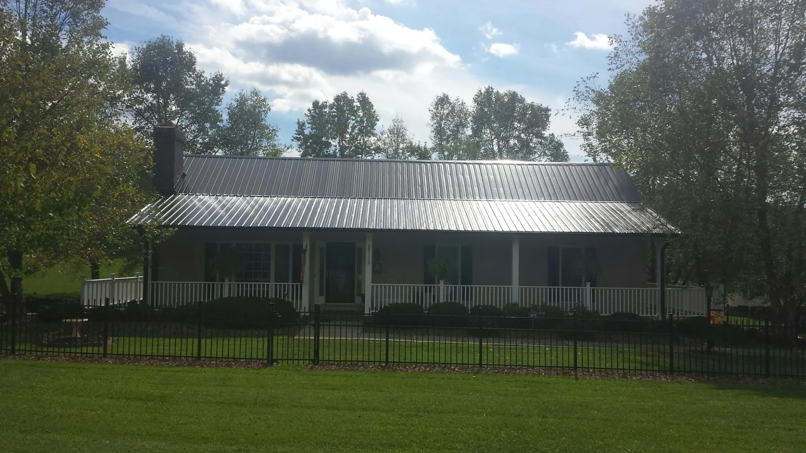 Gray metal roof on a brick ranch with a full width front porch — Gutter Guard Installation work by our crew in Caney