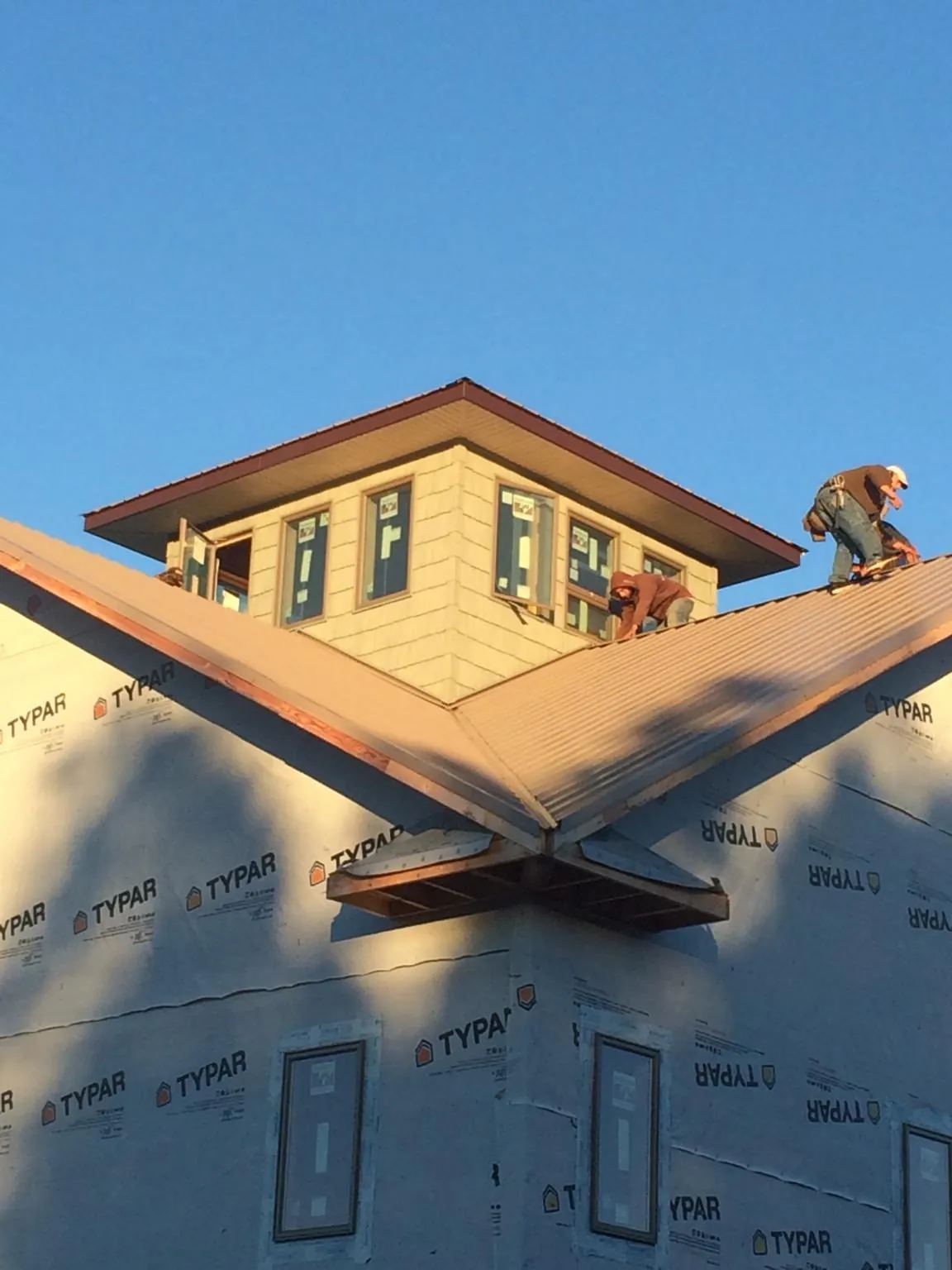 Roofers working around a rooftop cupola on a new metal roof at sunset — Roof Waterproofing in Caney by Roofing Brothers